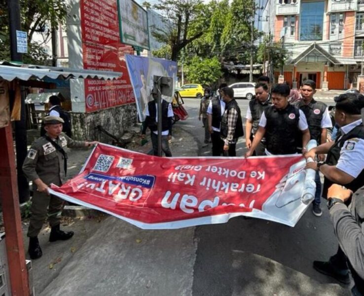 Petugas Satpol PP dan pegawai Bapenda Makassar melakukan penurunan paksa reklame yang terpampang diduga tanpa izin.